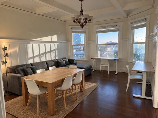 The shared area: a long table, sofas, and standing desks in the bay windows